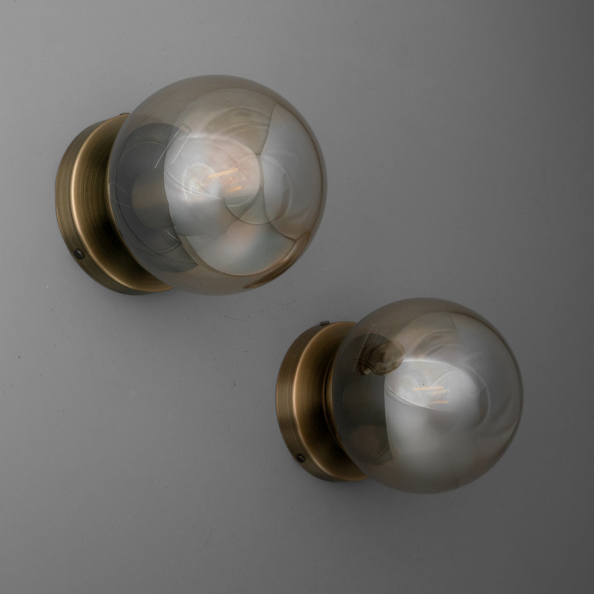 Pair of wall sconces with round smoky glass globes and antique brass circular mounts. - SCONCE MODEL NO. 1030