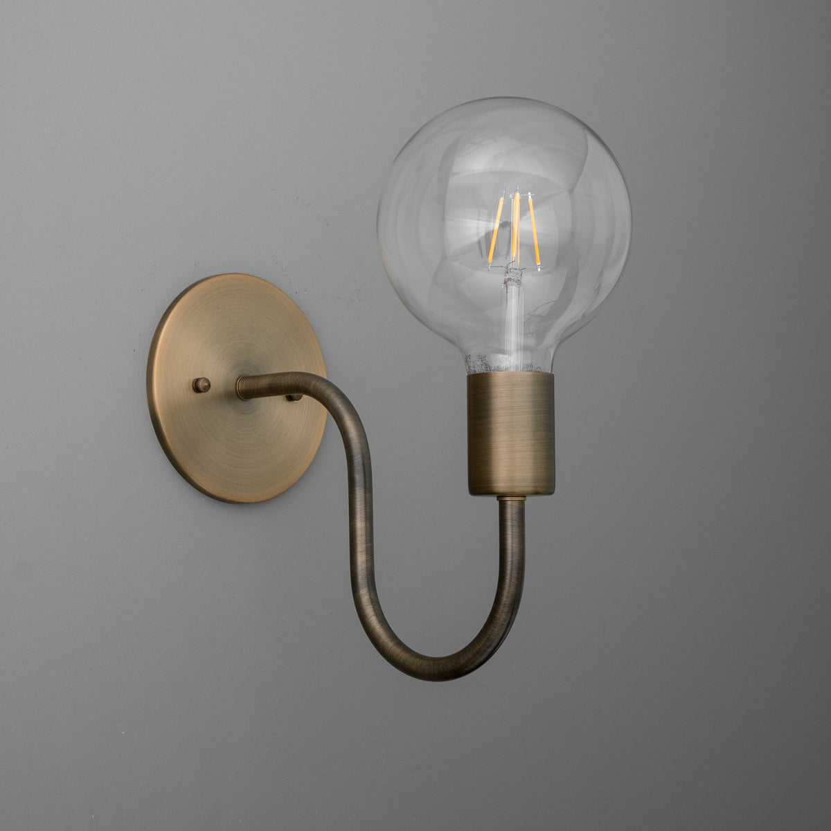 Wall-mounted sconce with antique brass round base and curved arm holding a clear globe bulb. - SCONCE MODEL NO. 4753