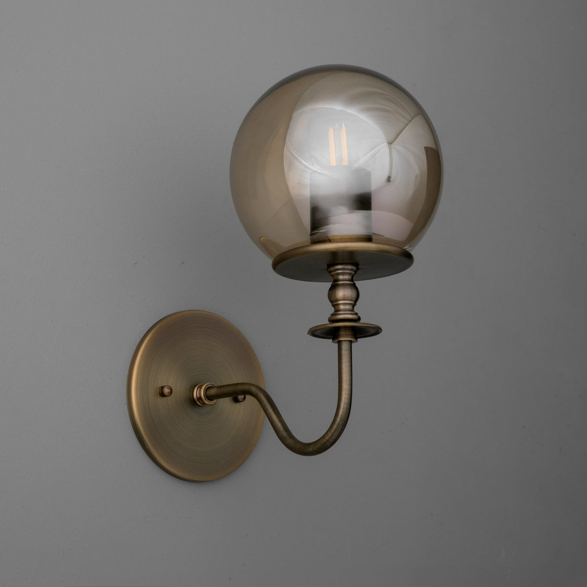 Wall sconce with antique brass finish and clear amber glass globe shade surrounding Edison bulb. - SCONCE MODEL NO. 1029