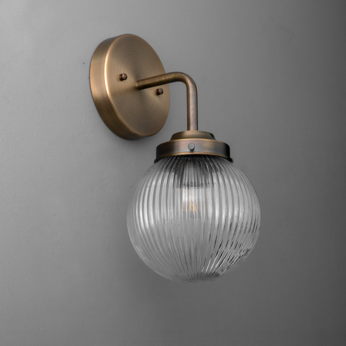 Wall sconce with ribbed clear glass globe and antique brass finish on curved arm and round backplate. - SCONCE MODEL NO. 6857