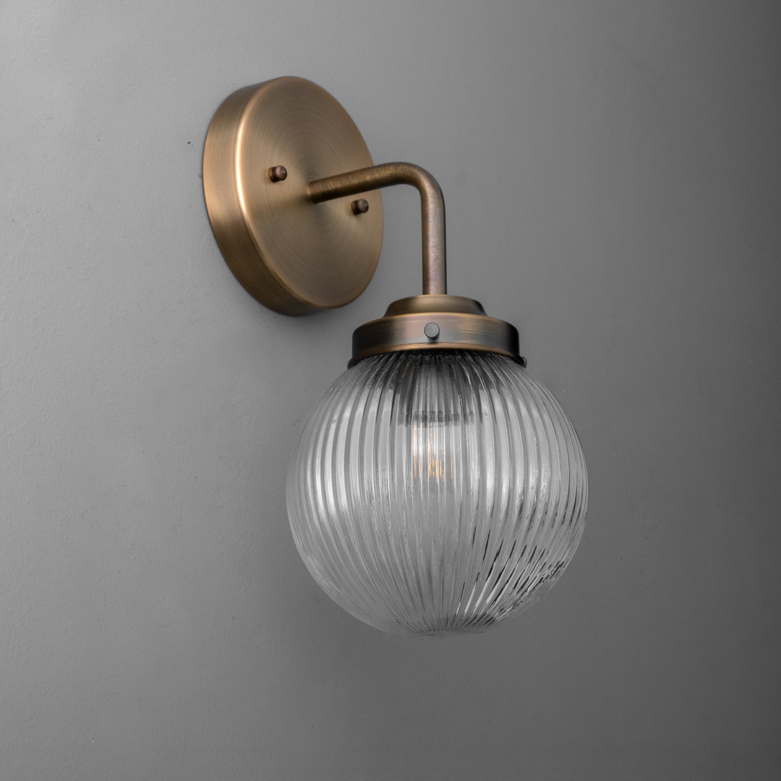 Wall sconce with ribbed clear glass globe and antique brass finish on curved arm and round backplate. - SCONCE MODEL NO. 6857