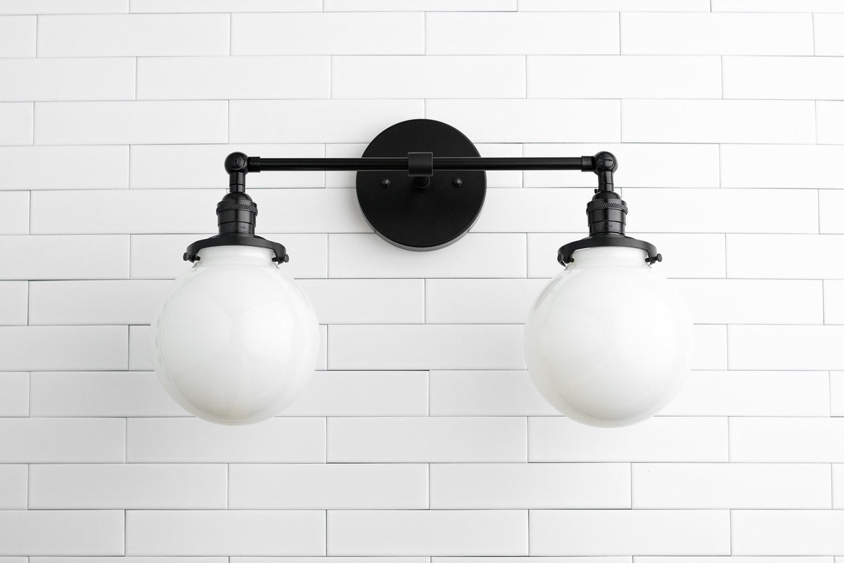 Industrial black metal vanity light with two white globe bulbs mounted on white tiled wall. - VANITY LIGHT MODEL NO. 5348