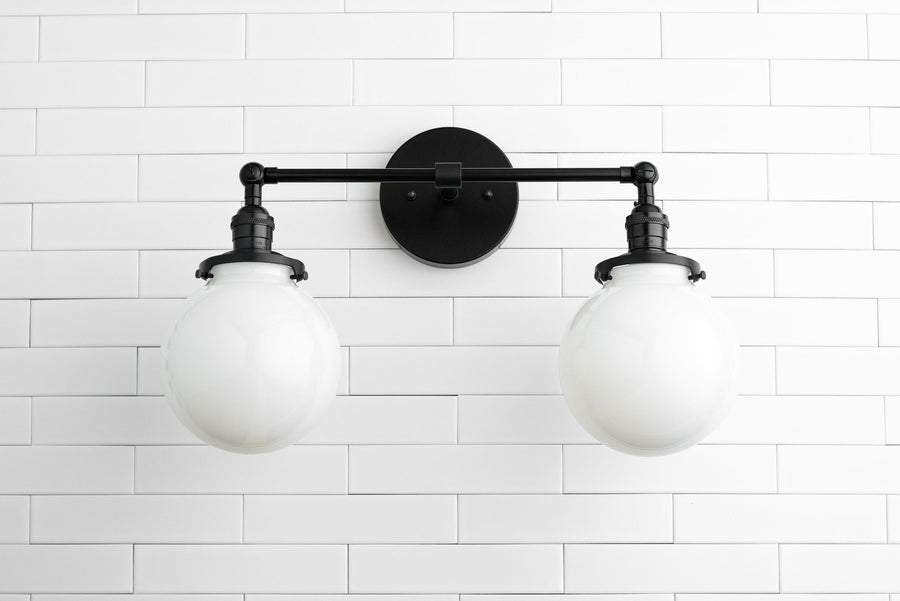 Industrial black metal vanity light with two white globe bulbs mounted on white tiled wall. - VANITY LIGHT MODEL NO. 5348