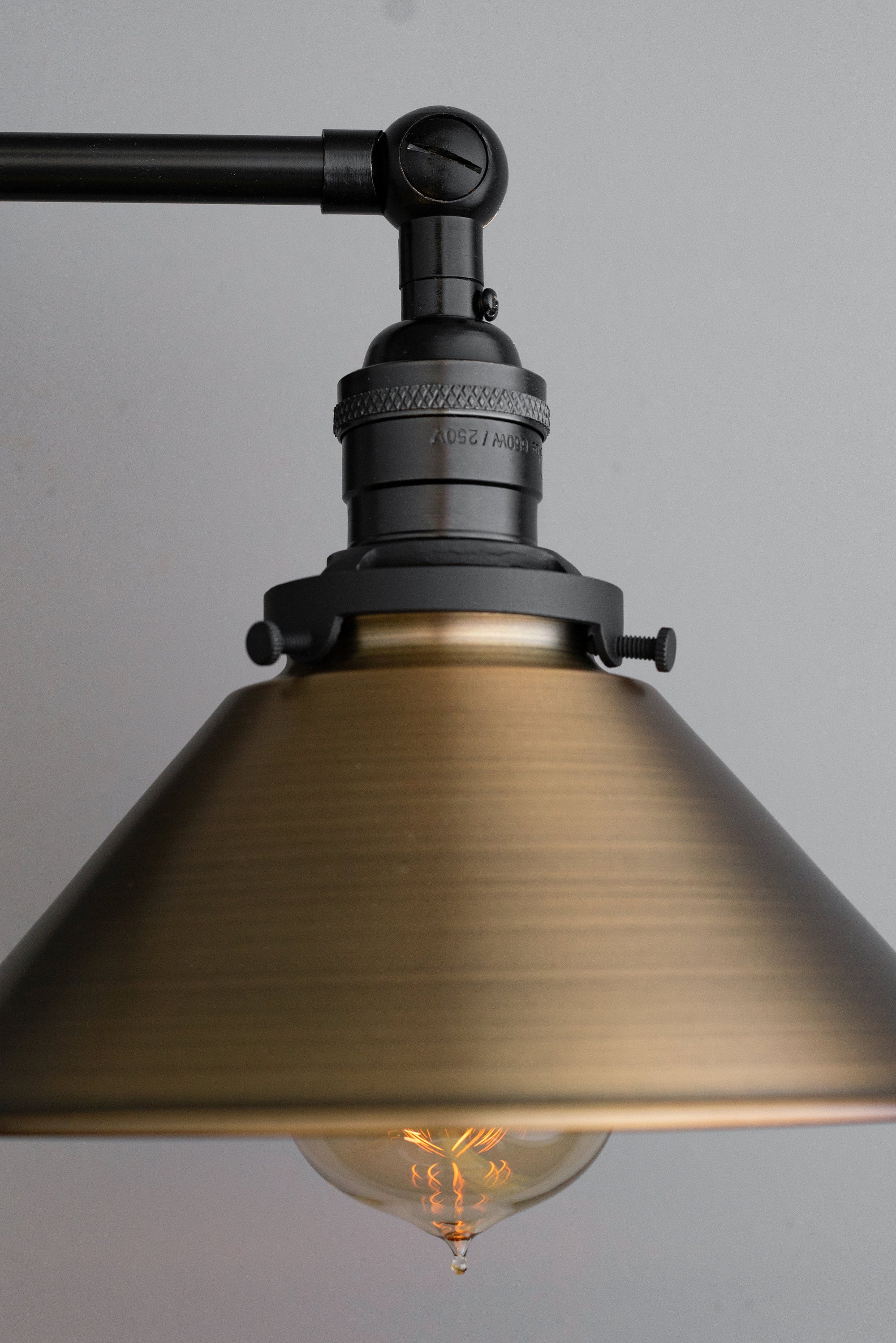 Industrial-style vanity light with black metal arm and antique brass conical shade, glowing filament bulb. - VANITY LIGHT MODEL NO. 1861