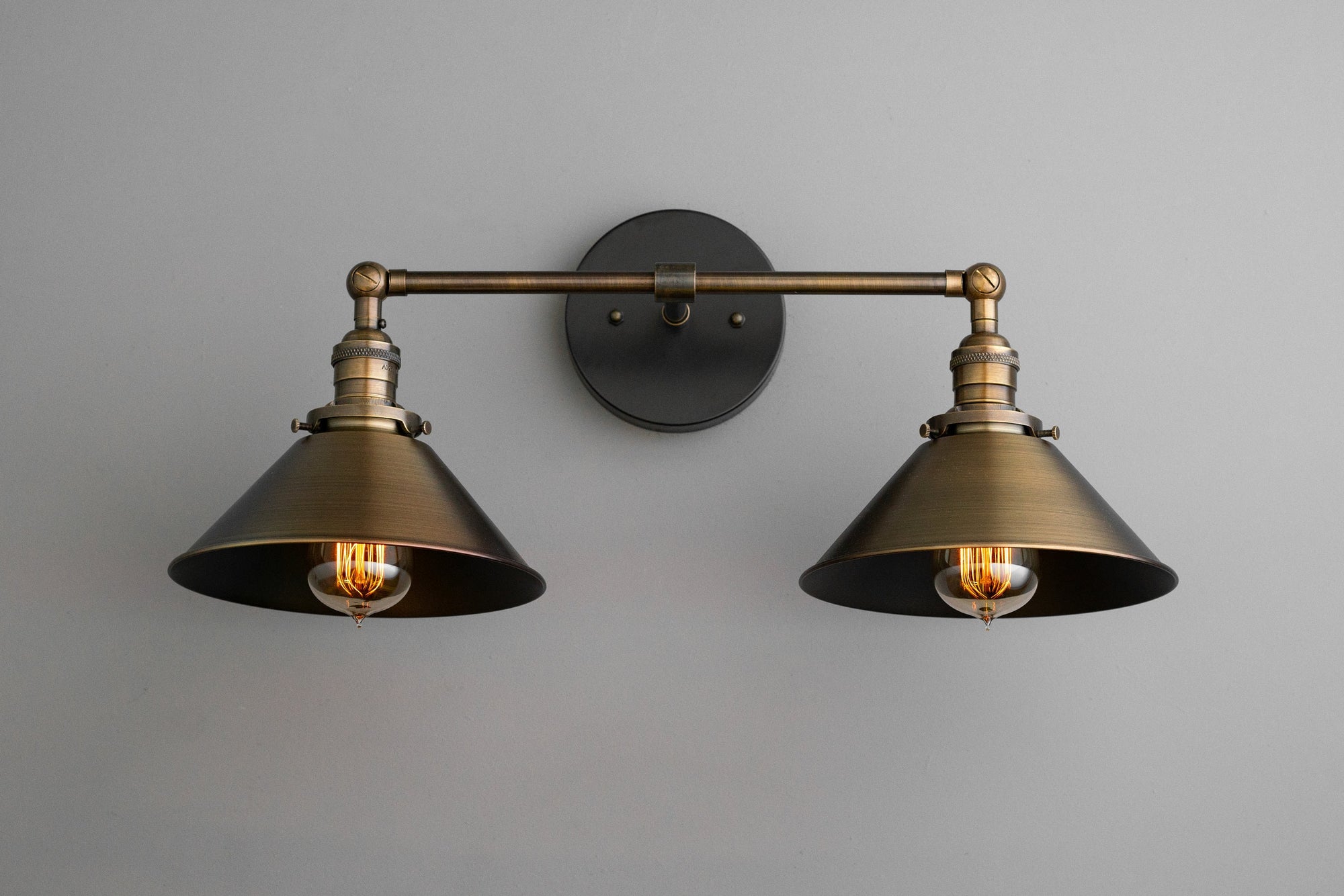 Two-bulb industrial vanity light with black metal shades and antique brass fixture mounted on gray wall. - VANITY LIGHT MODEL NO. 1861