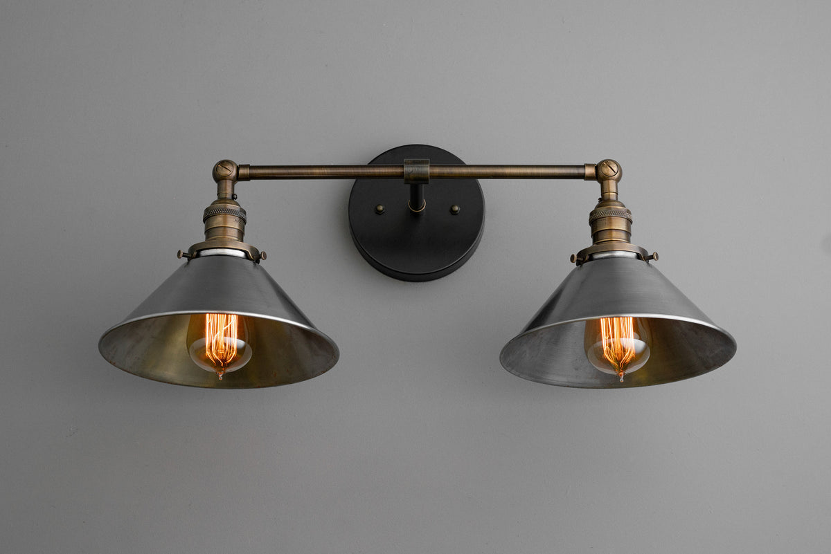 Two-bulb industrial vanity light with black metal shades and antique brass finish on gray wall. - VANITY LIGHT MODEL NO. 0799
