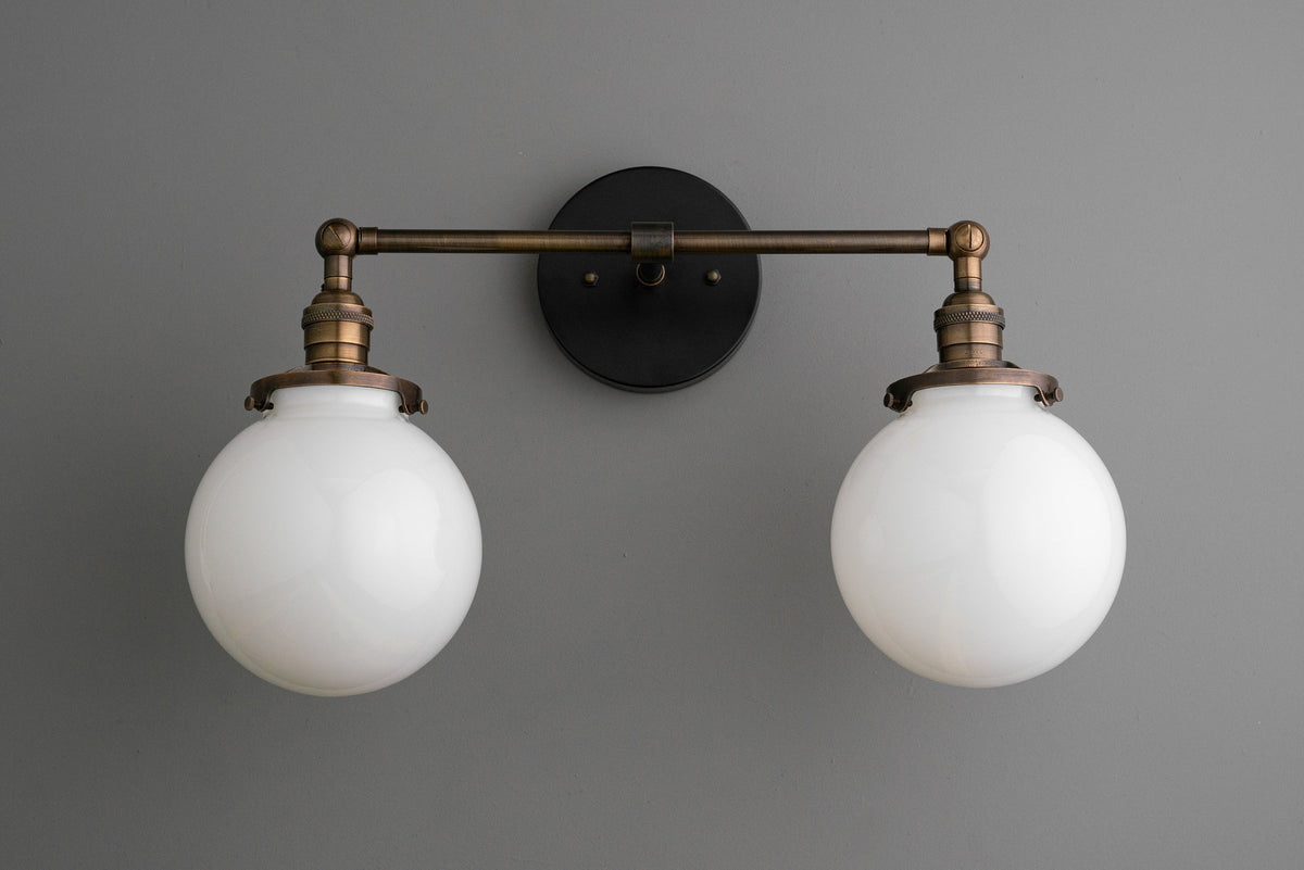 Industrial-style wall vanity light with two white glass globe shades and antique brass finish. - VANITY LIGHT MODEL NO. 5348