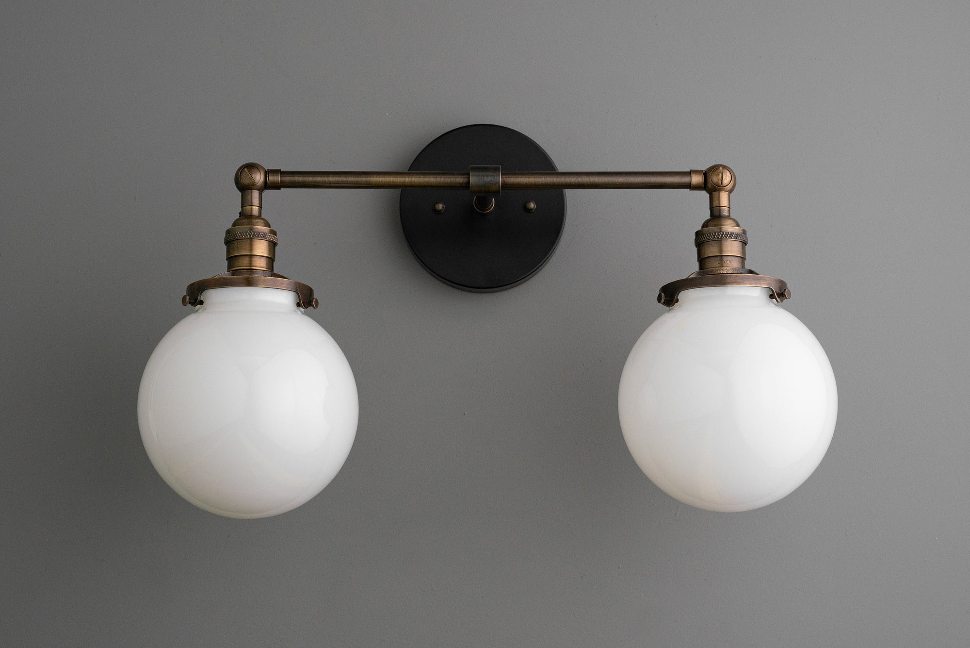 Industrial-style wall vanity light with two white glass globe shades and antique brass finish. - VANITY LIGHT MODEL NO. 5348
