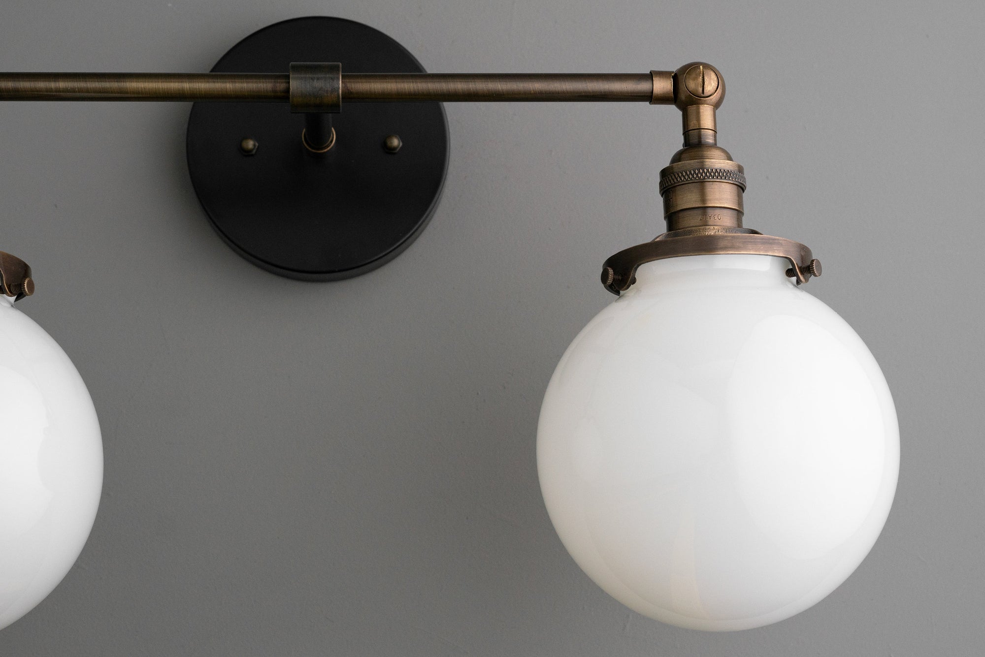 Industrial style vanity light with round white globe shade and antique brass finish mounting arm on gray wall. - VANITY LIGHT MODEL NO. 5348