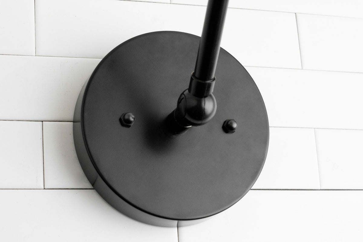 Matte black round wall sconce base with adjustable arm mounted on white subway tile wall. - SCONCE MODEL NO. 8551