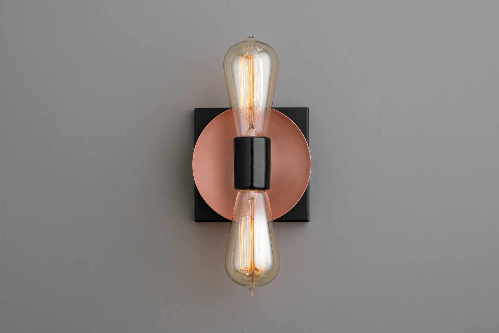 Industrial wall sconce with black base and copper circular backplate featuring two exposed filament bulbs up and down. - SCONCE MODEL NO. 8169