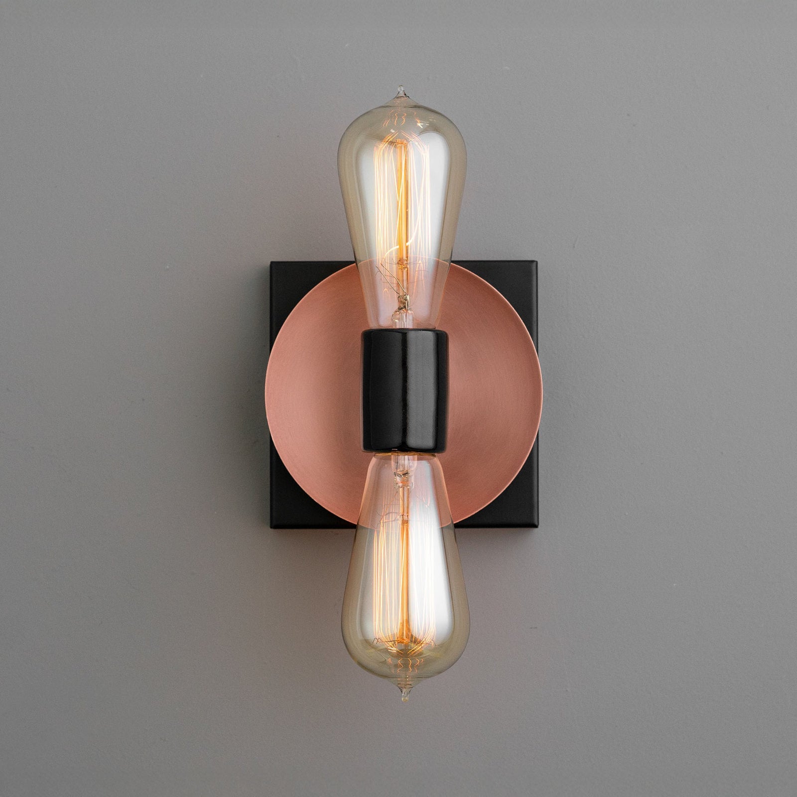 Industrial-style wall sconce with exposed vintage filament bulbs, copper backplate, and black accents. - SCONCE MODEL NO. 8169