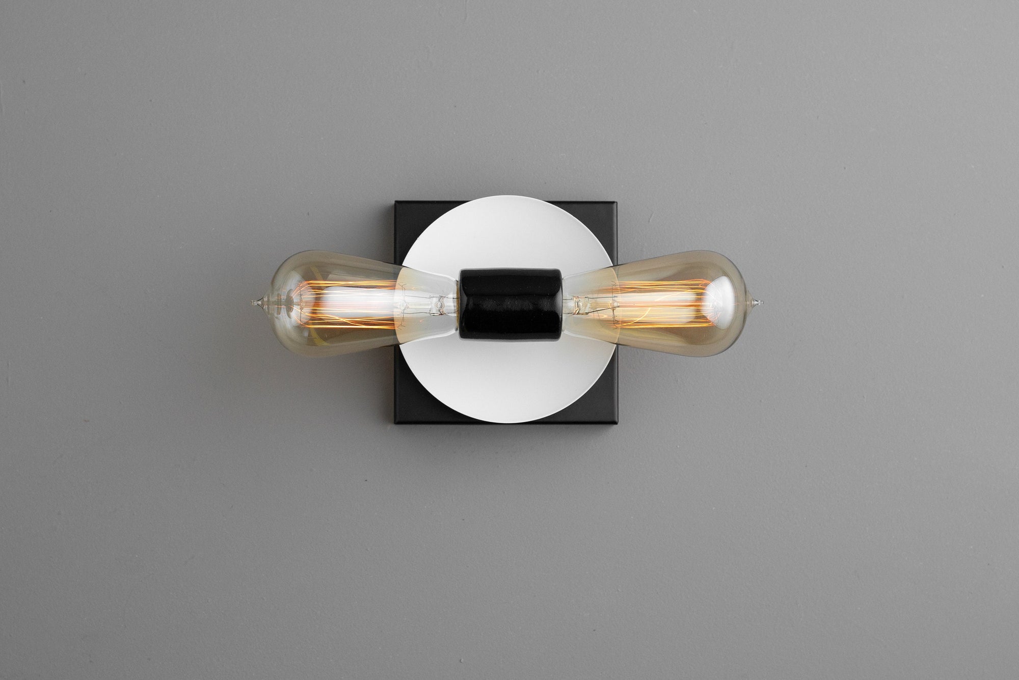 Industrial-style black metal wall sconce with exposed filament bulbs and white circular backplate. - SCONCE MODEL NO. 8169