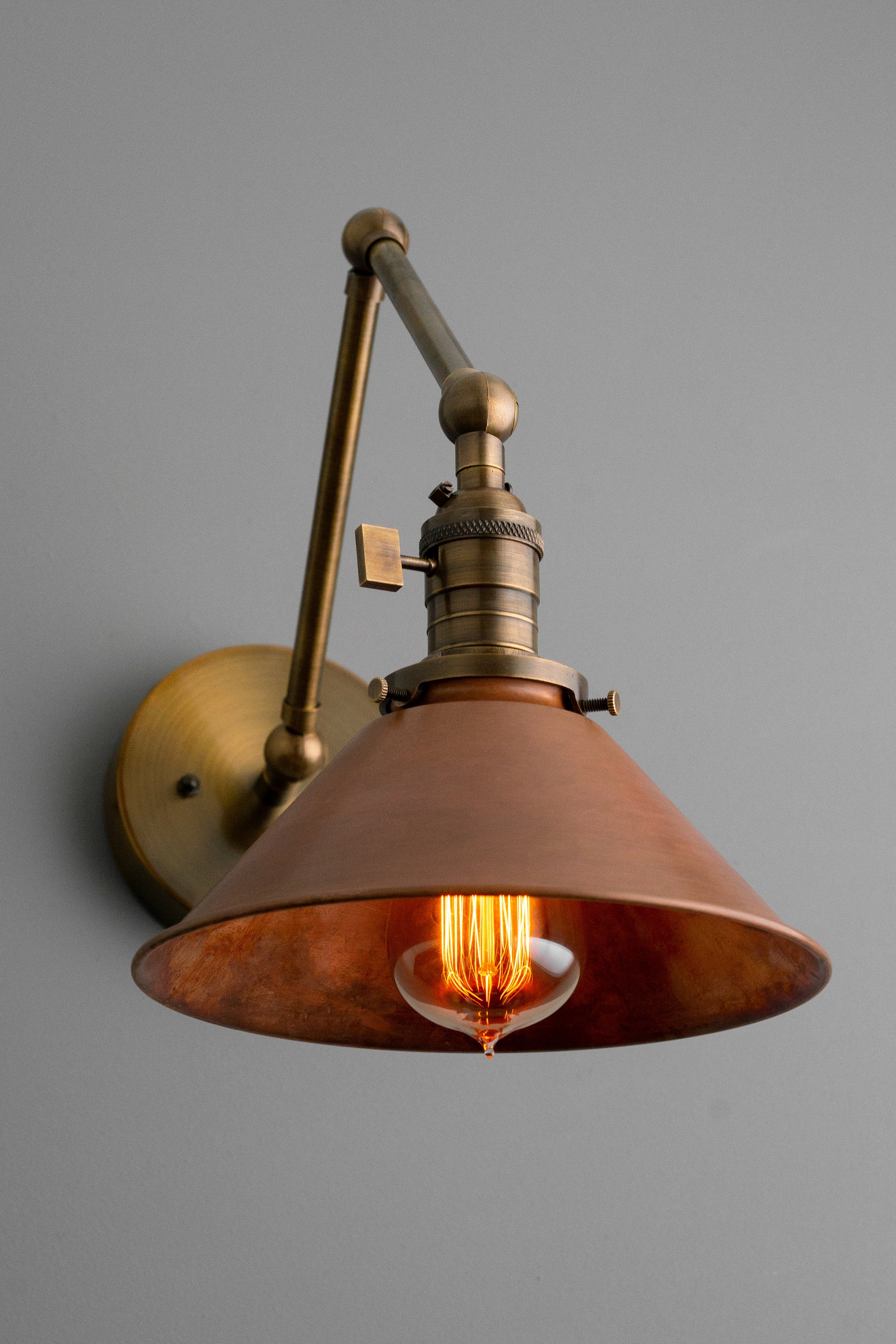 Industrial adjustable wall sconce in antique brass with conical metal shade and exposed filament bulb. - SCONCE MODEL NO. 6668
