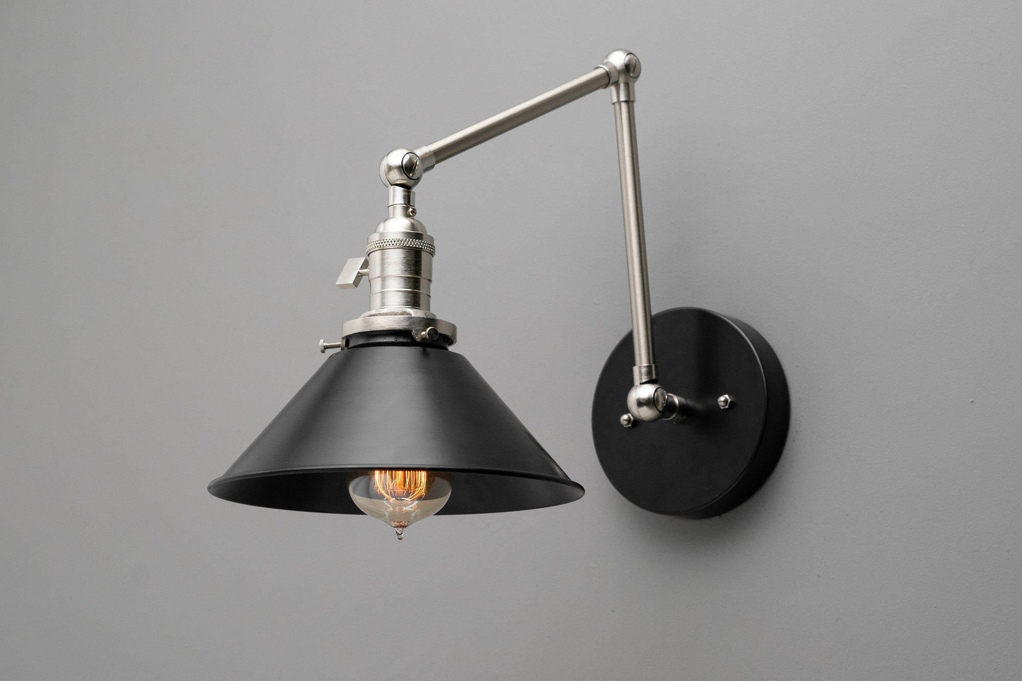 Adjustable industrial wall sconce with black metal conical shade and brushed nickel arm on grey background. - SCONCE MODEL NO. 7164