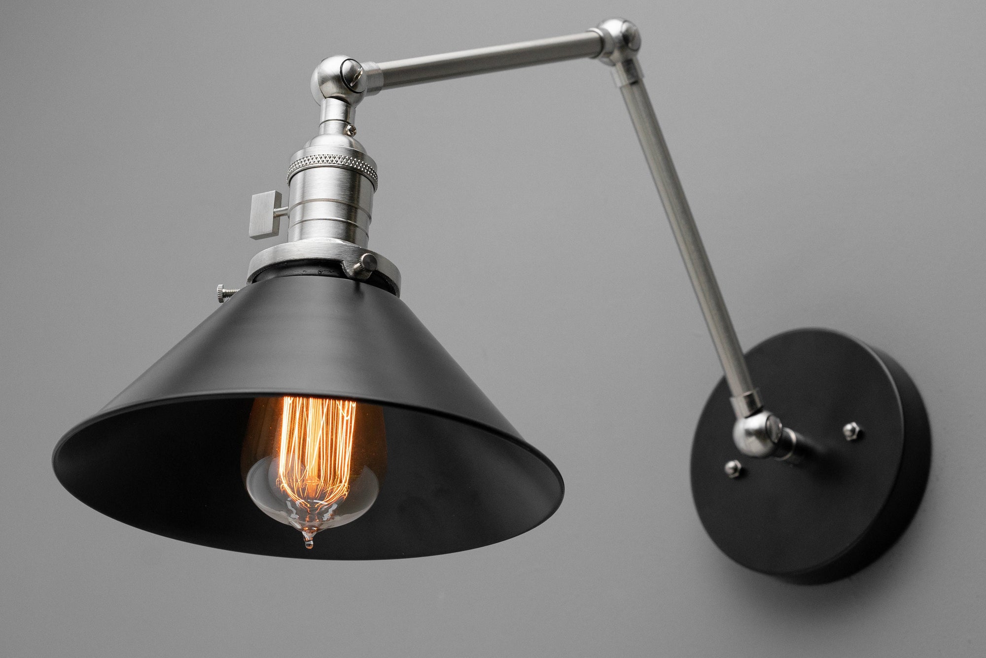 Industrial-style adjustable wall sconce with matte black shade and brushed nickel arm on gray background. - SCONCE MODEL NO. 7164