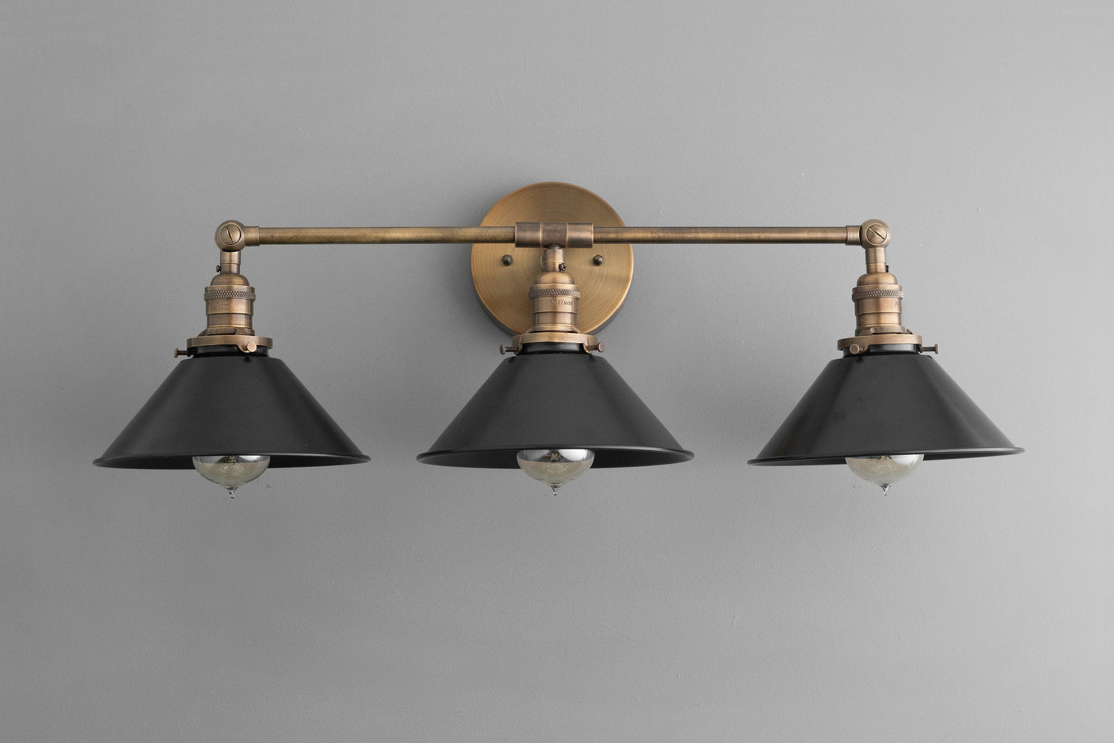 Three-bulb industrial vanity light with antique brass finish and black metal shades mounted on a round wall plate. - VANITY LIGHT MODEL NO. 3406