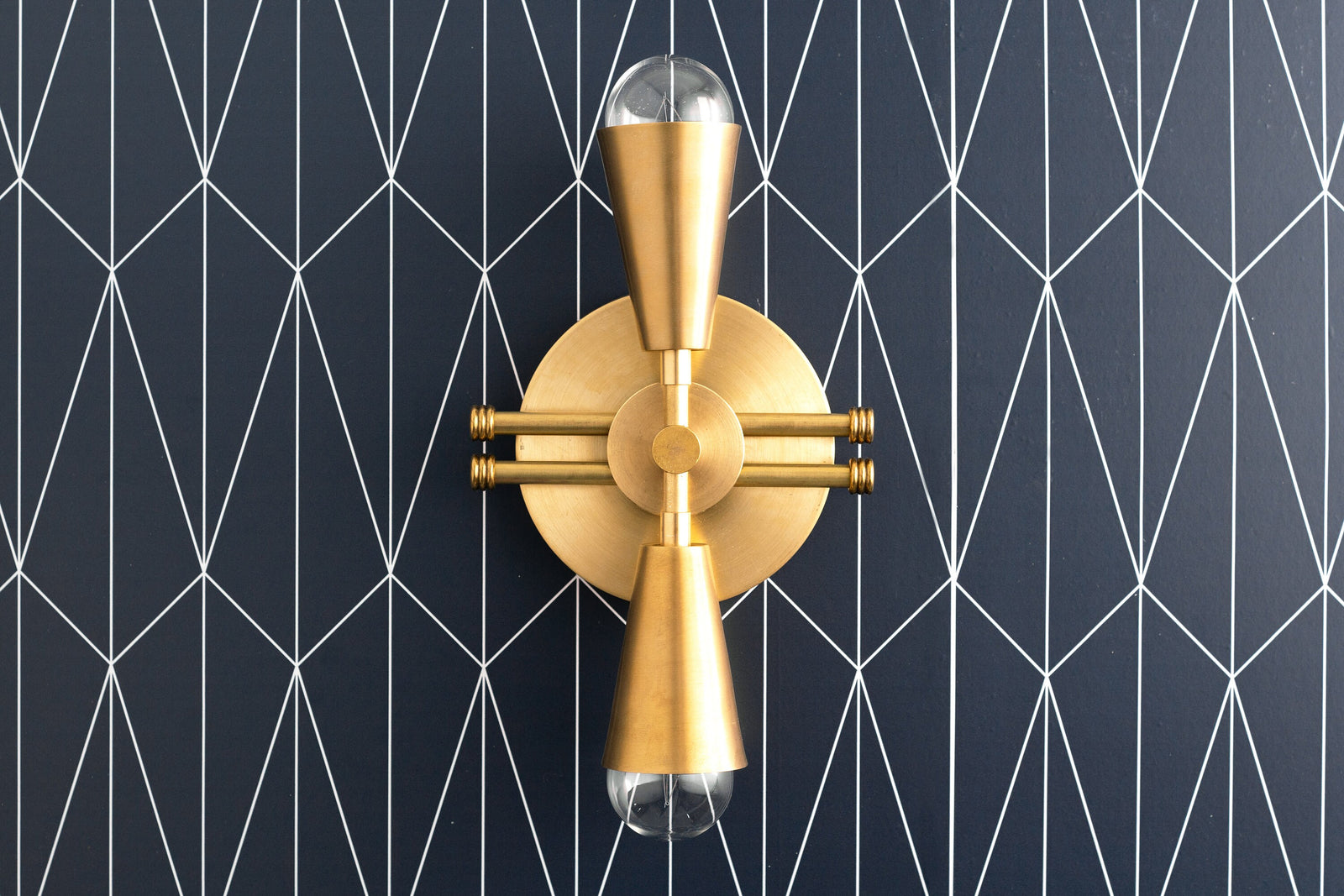 Art Deco raw brass wall sconce with exposed bulbs and geometric mounting plate on black patterned wall. - SCONCE MODEL NO. 3419