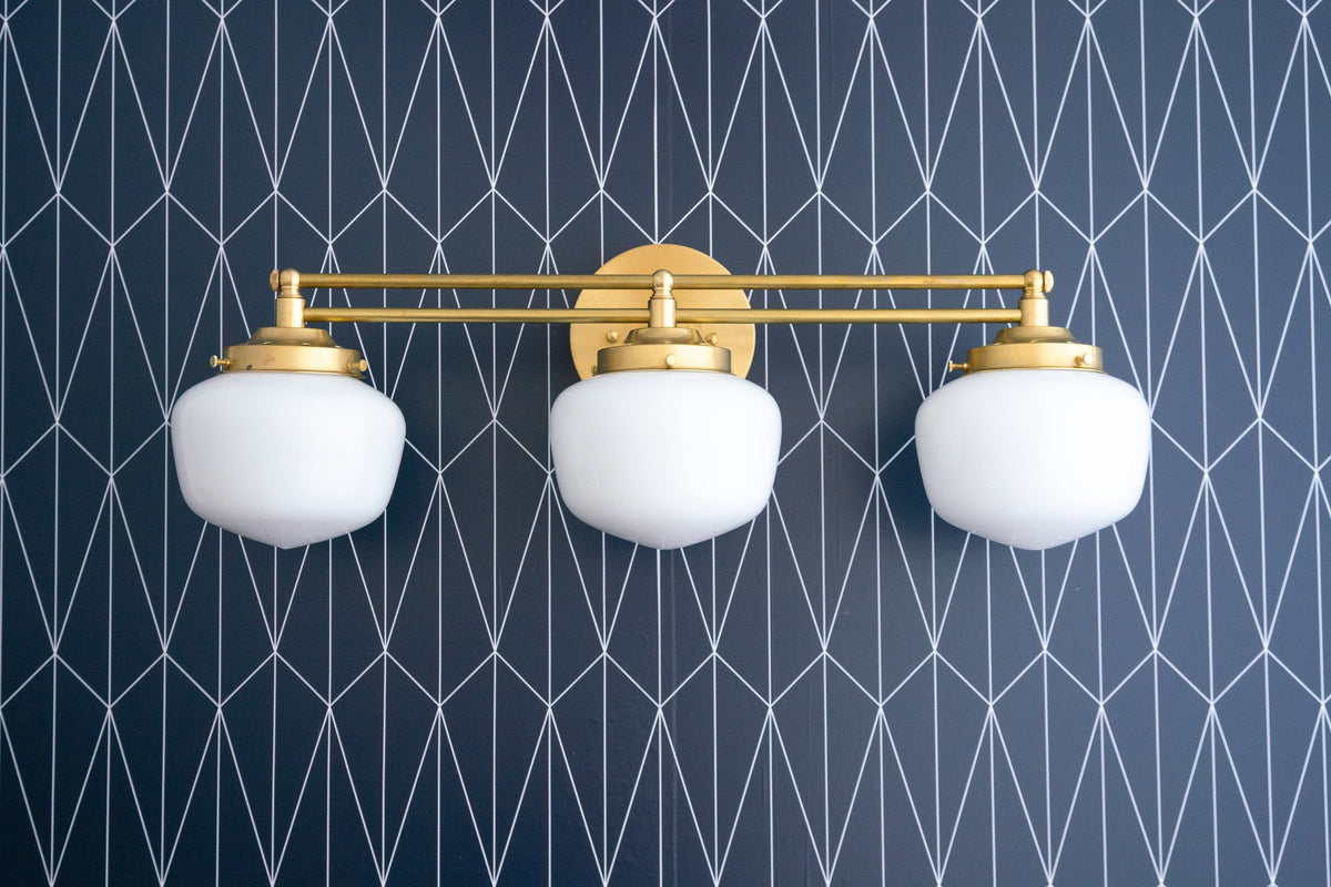 Art Deco 3-bulb vanity light with frosted white globes and raw brass finish mounted on geometric navy wallpaper. - VANITY LIGHT MODEL NO. 4352