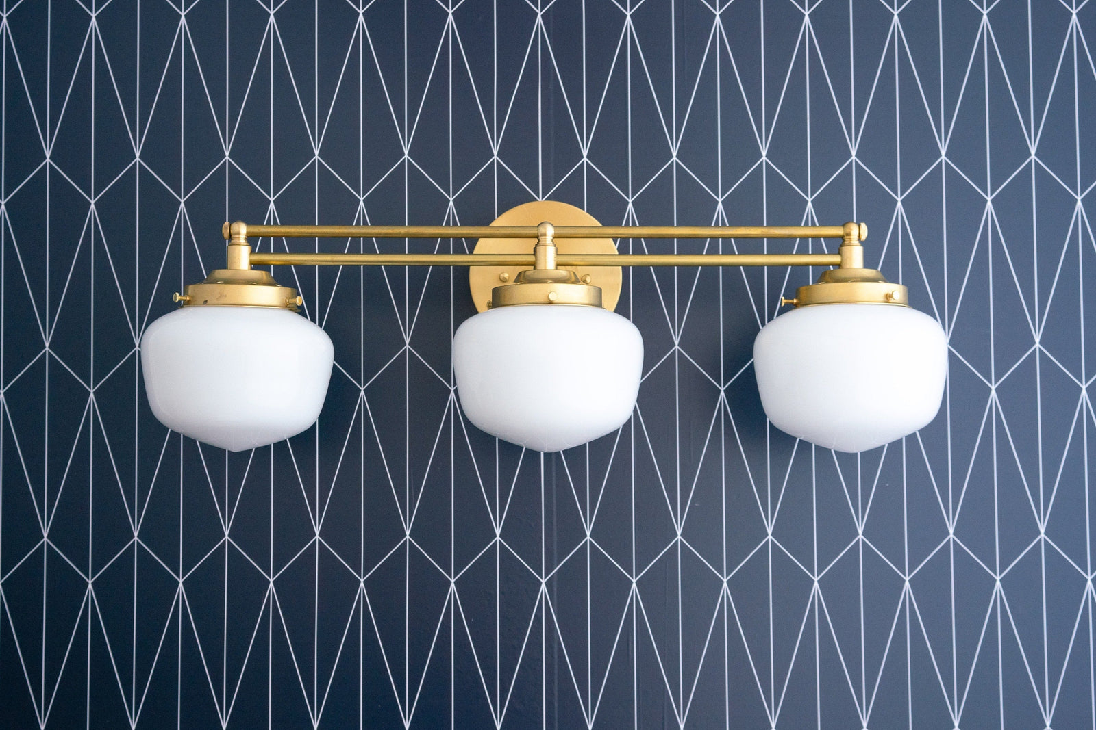 Art Deco 3-bulb vanity light with frosted white globes and raw brass finish mounted on geometric navy wallpaper. - VANITY LIGHT MODEL NO. 4352