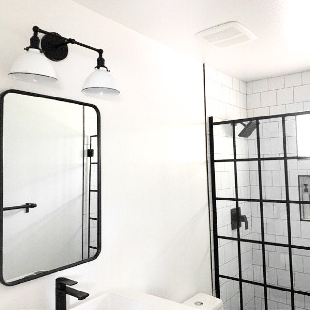 Black industrial 2-bulb vanity light with white metal shades mounted above rectangular black-framed mirror. - VANITY LIGHT MODEL NO. 4564