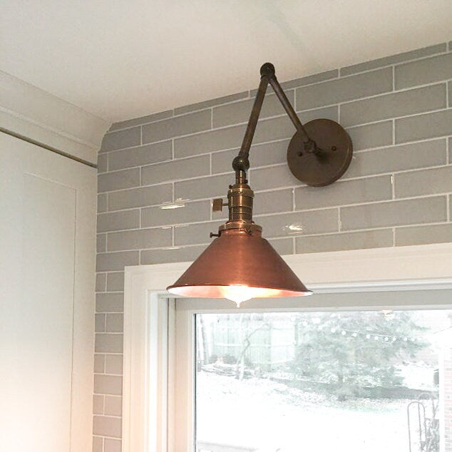 Industrial adjustable wall sconce with a copper-toned conical shade and dark metal arm mounted on gray subway tile wall. - SCONCE MODEL NO. 6668