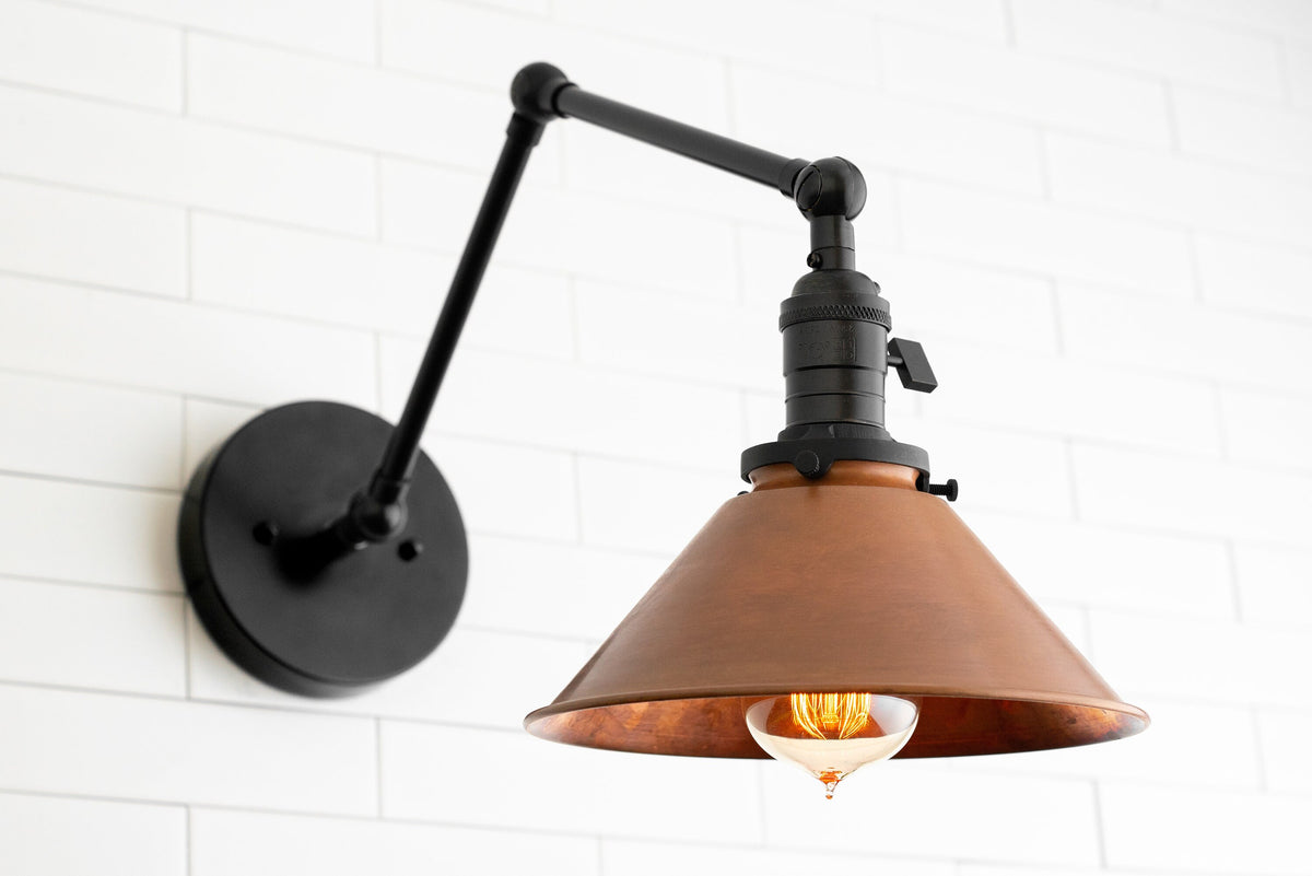 Adjustable industrial wall sconce with raw brass cone shade and black arm mounted on white brick wall. - SCONCE MODEL NO. 6668