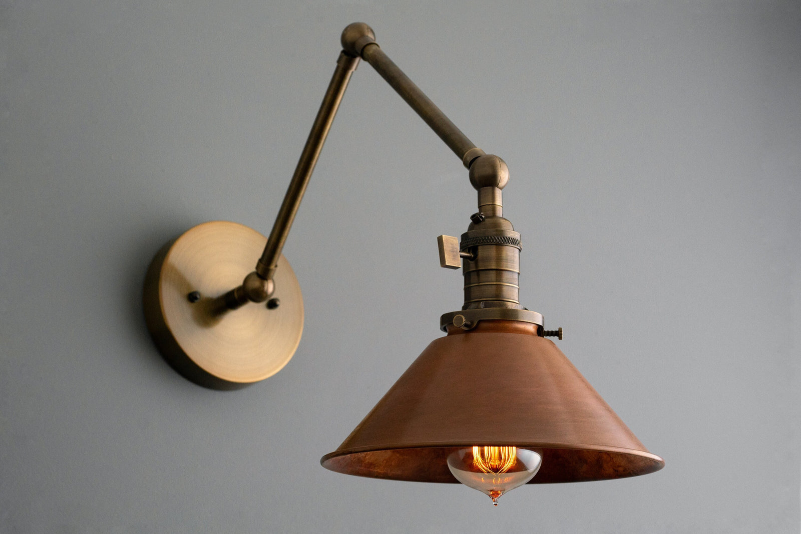 Adjustable industrial wall sconce with raw brass arm and copper cone shade, vintage bulb visible. - SCONCE MODEL NO. 6668