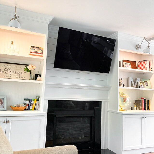 Adjustable brushed nickel wall sconce with a conical metal shade mounted above a white built-in bookshelf and fireplace. - SCONCE MODEL NO. 8551