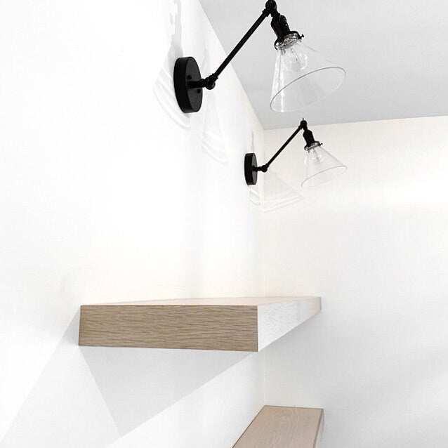 Black adjustable industrial wall sconces with clear glass cone shades mounted above floating wooden shelves. - SCONCE MODEL NO. 7962