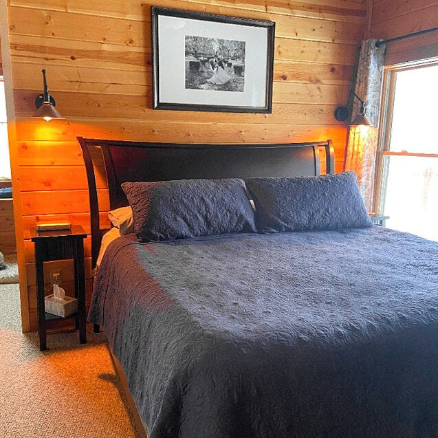 Adjustable black industrial wall sconce with metal shade, mounted above wooden bedside table and bed. - SCONCE MODEL NO. 6668