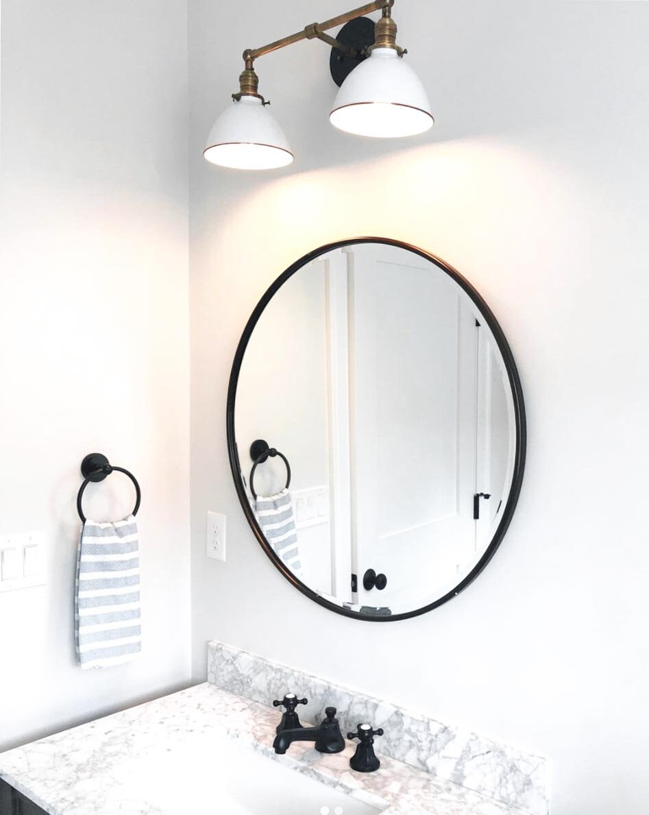 Black industrial 2-bulb vanity light with white metal shades mounted above round mirror. - VANITY LIGHT MODEL NO. 4564