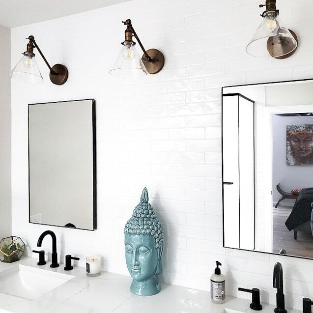 Adjustable industrial-style wall sconces in antique brass with clear glass shades above bathroom mirrors. - SCONCE MODEL NO. 7962