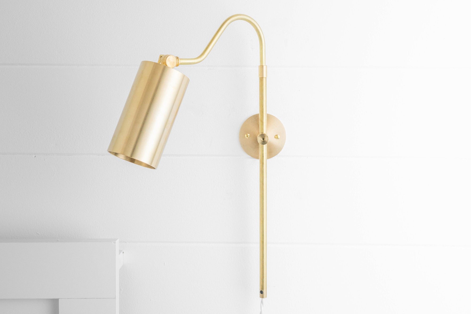 Adjustable sealed brass mid-century modern wall sconce with cylindrical shade and white cord plugged in. - SCONCE MODEL NO. 1132
