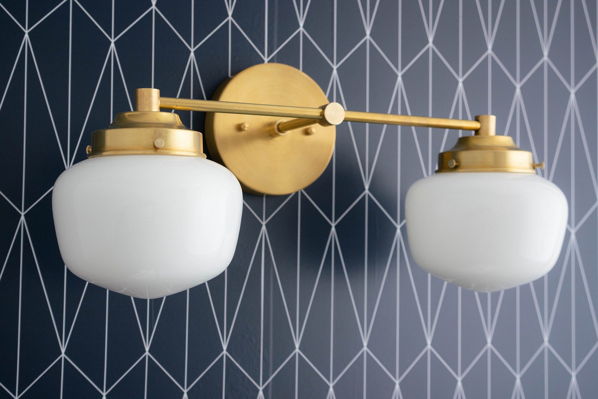 Mid-century modern two-bulb vanity light with white globe shades and antique brass finish mounted on geometric navy blue wall. - VANITY LIGHT MODEL NO. 5799