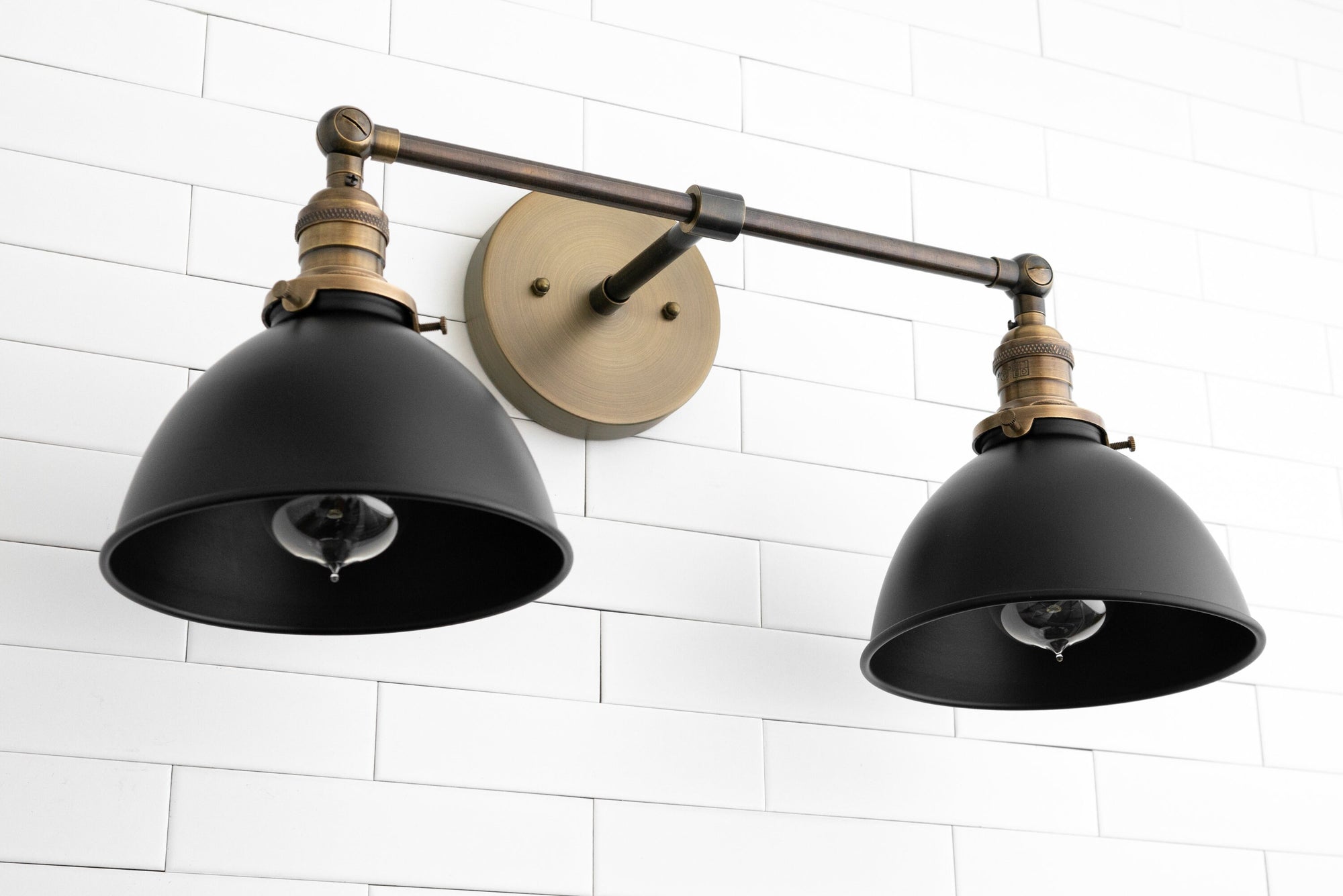 Industrial 2-light black metal wall sconce with adjustable arms and brass accents mounted on white tile wall. - SCONCE MODEL NO. 8791