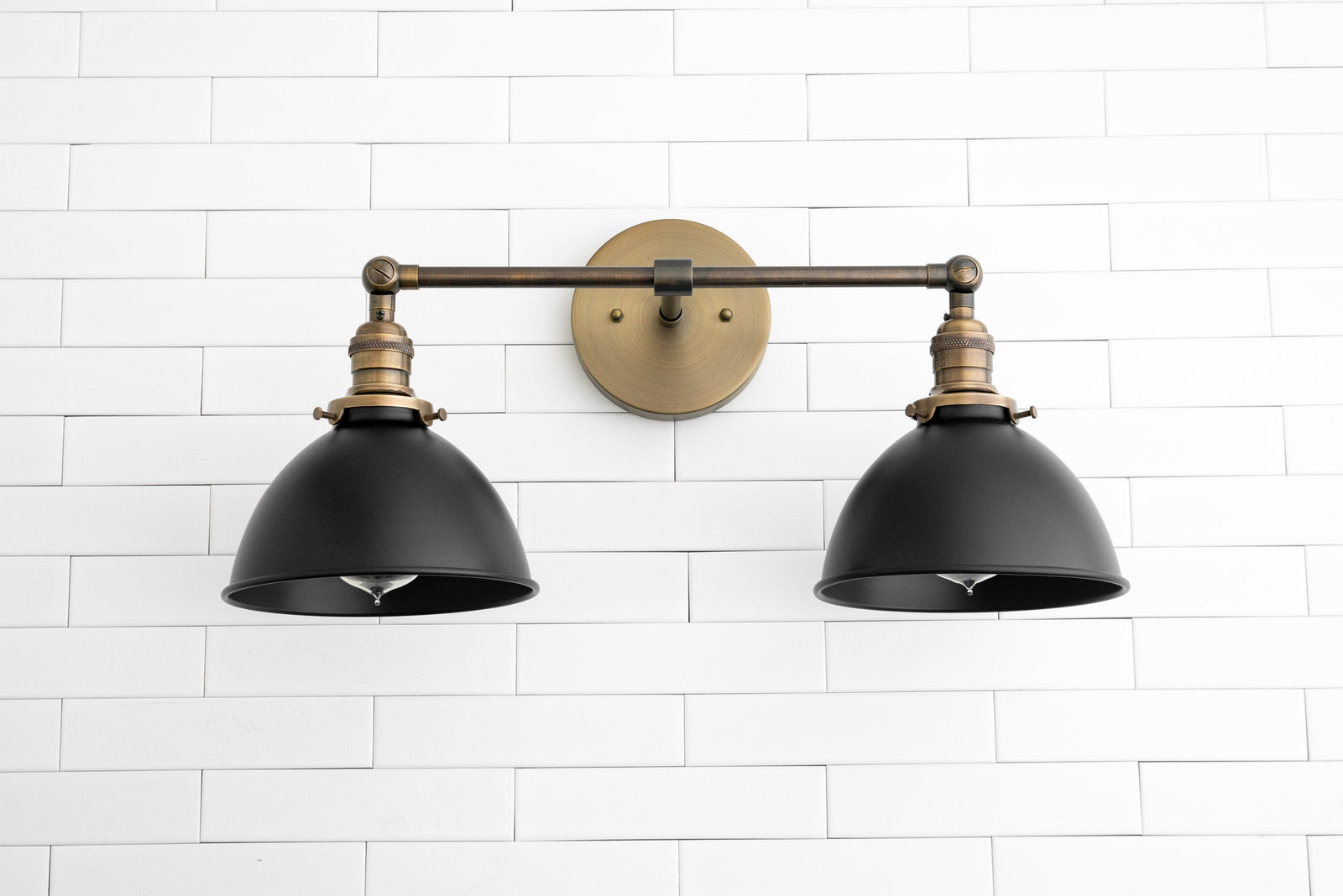 Industrial style 2-light vanity sconce with black shades and antique brass fixture mounted on white tile wall. - SCONCE MODEL NO. 8791