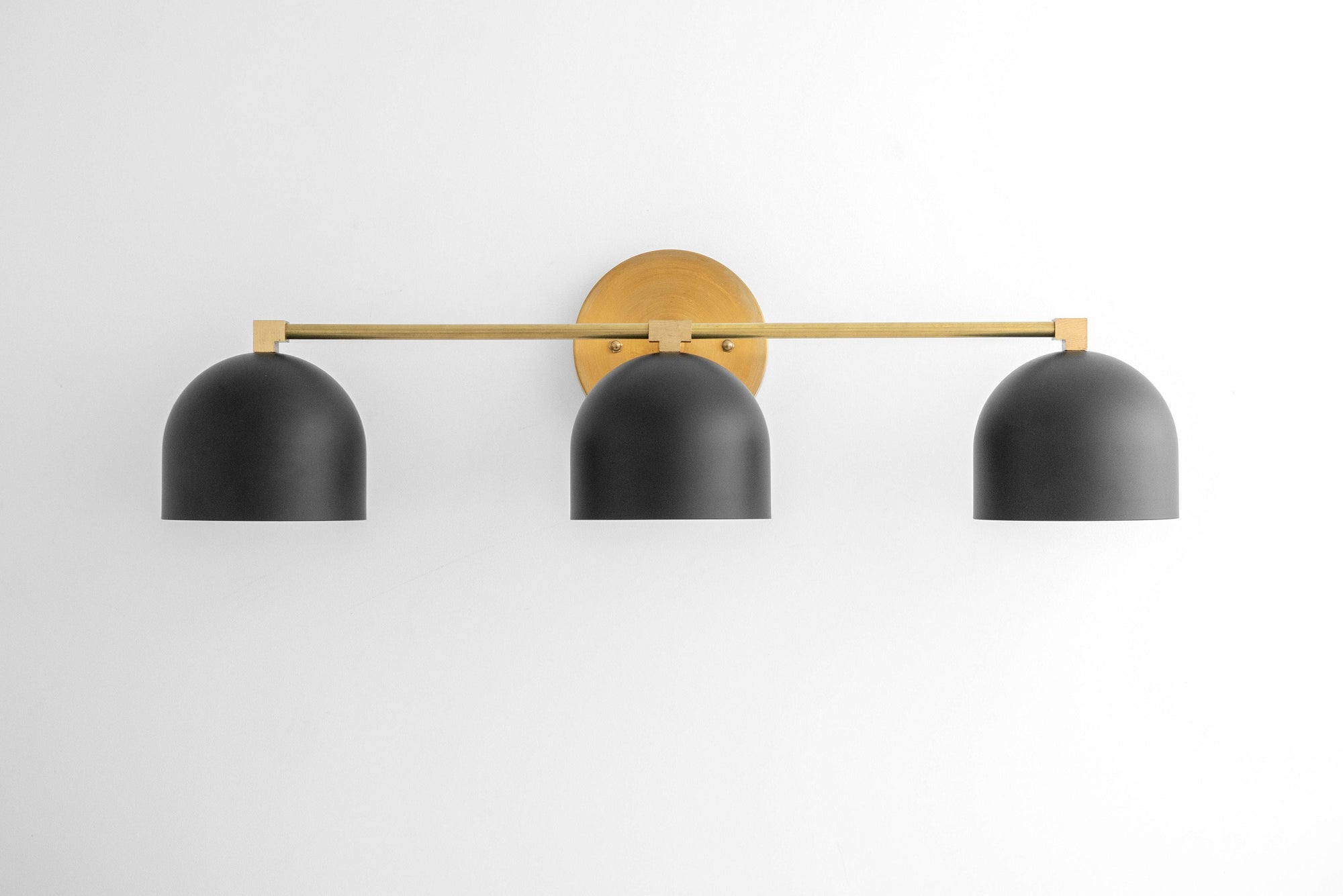 Mid-century modern vanity light with three matte black dome shades and a brass horizontal bar mounting on white wall. - VANITY LIGHT MODEL NO. 7565
