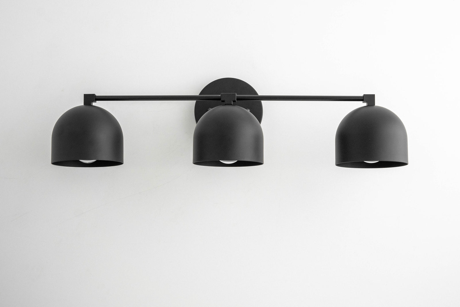 Black three-bulb vanity light with matte dome-shaped shades and slim horizontal bar mounting. - VANITY LIGHT MODEL NO. 7565