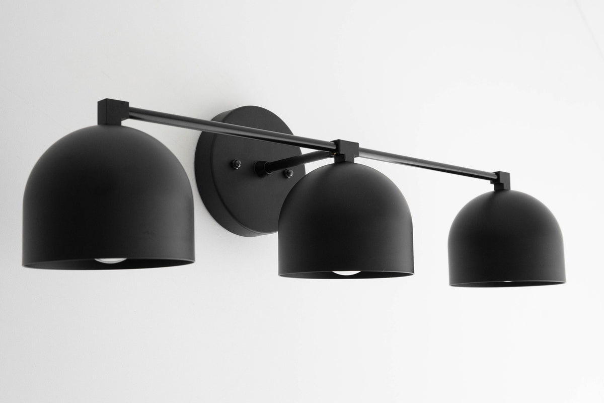 Three-bulb matte black mid-century modern vanity light with dome-shaped shades and a circular wall mount. - VANITY LIGHT MODEL NO. 7565