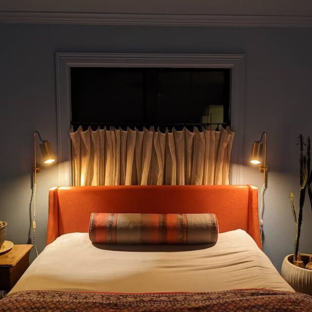 Pair of adjustable mid-century modern brass and black metal wall sconces with cone shades above a bed with rust orange. - SCONCE MODEL NO. 1132
