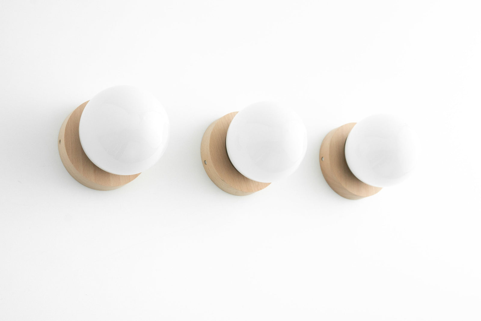 Three Scandinavian-style wall sconces with matte white globe shades and natural wood bases mounted in a row on a white wall. - SCONCE MODEL NO. 5719