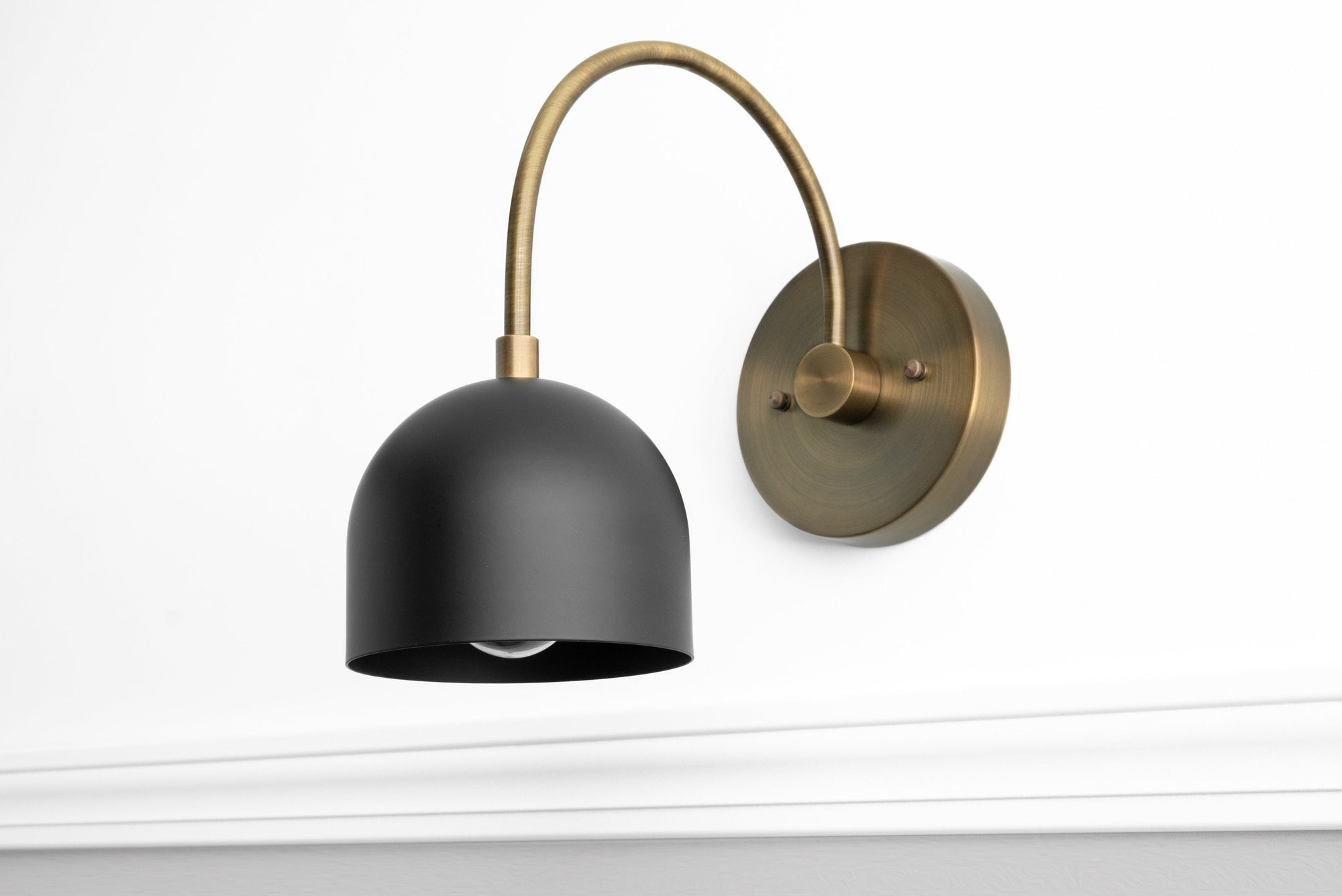 Mid-century modern black metal sconce with curved antique brass arm and round wall mount. - SCONCE MODEL NO. 8586