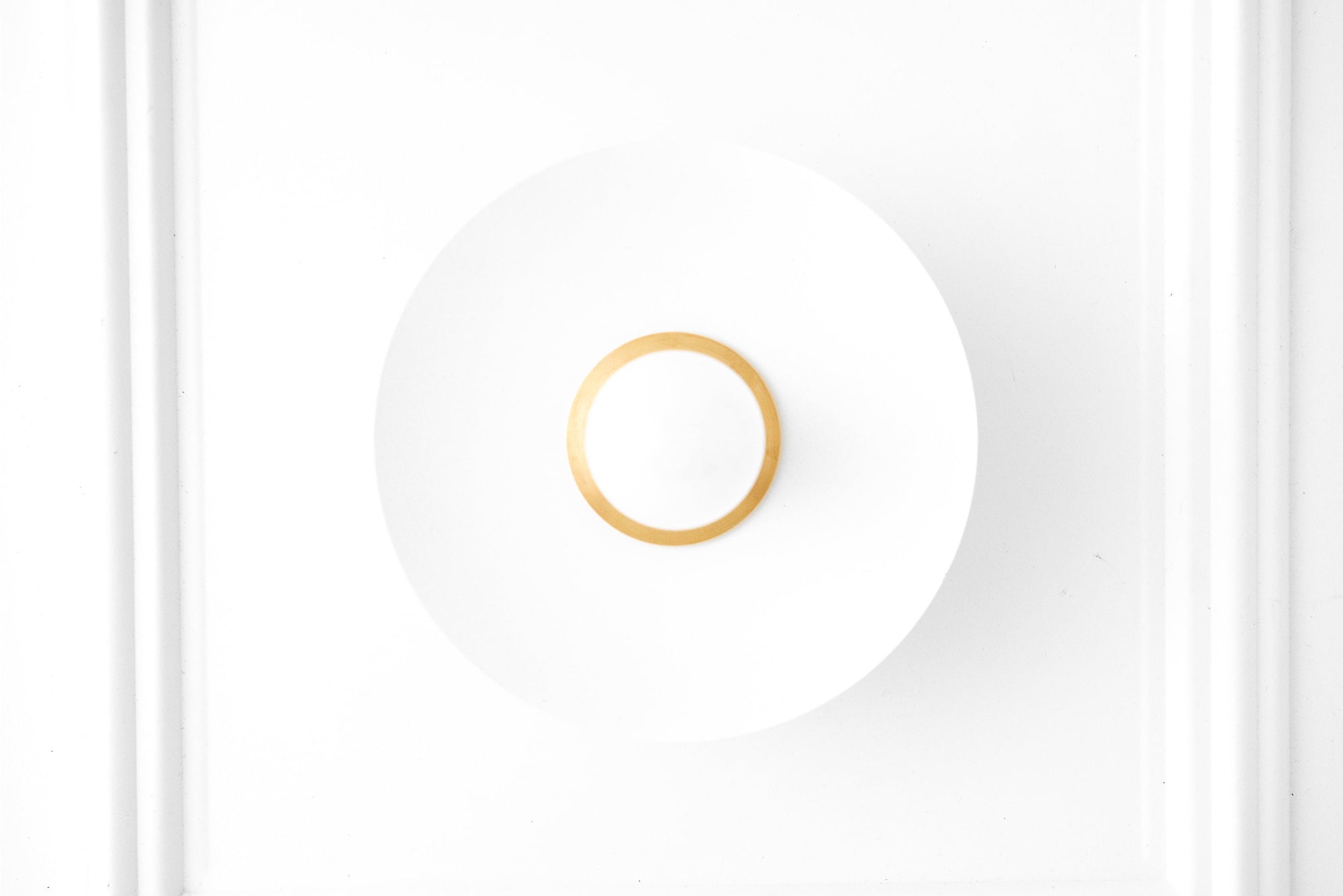 Scandinavian-style wall sconce with raw brass ring and frosted white glass shade flush mounted on white wall. - SCONCE MODEL NO. 9660