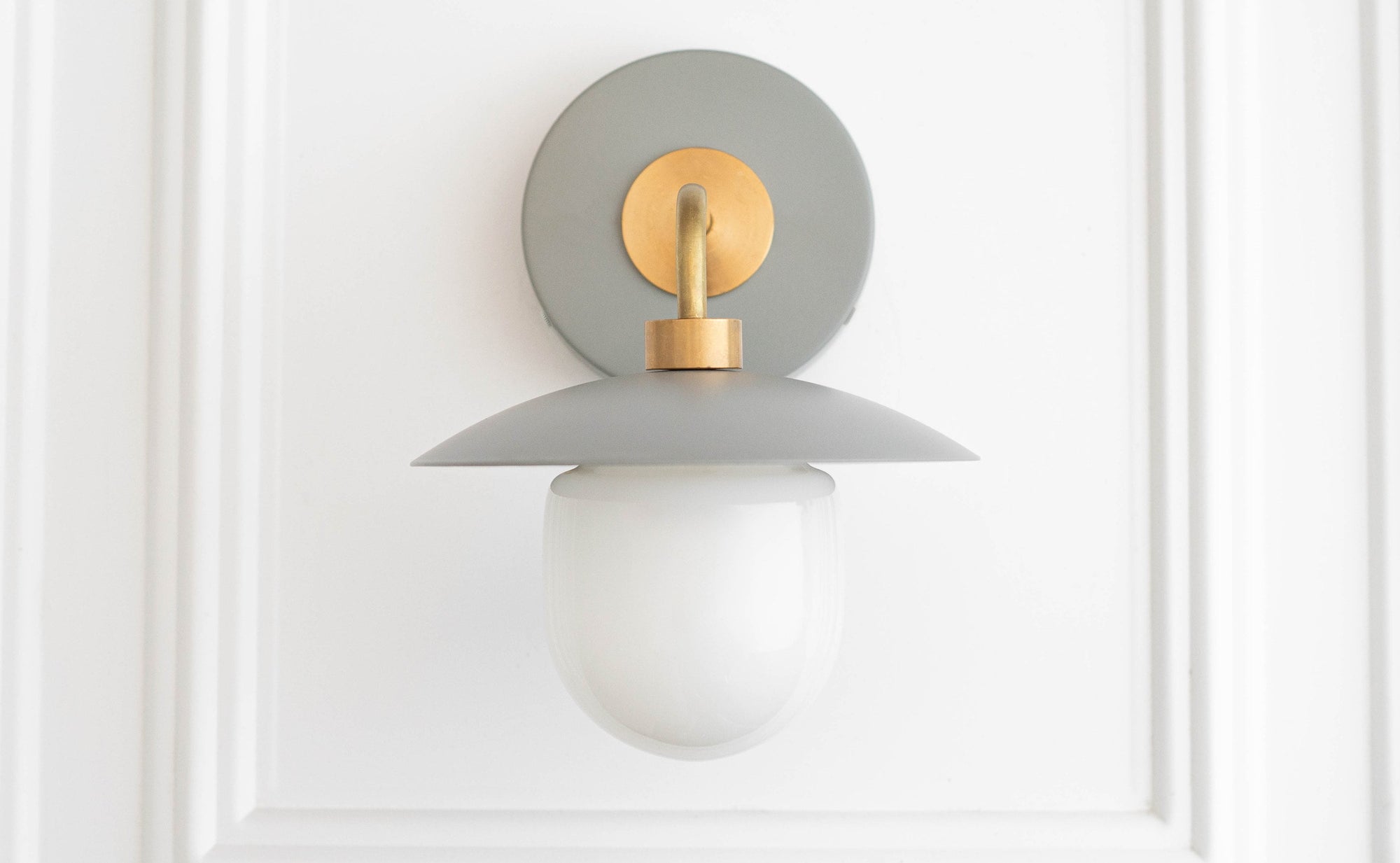 Mid-century modern wall sconce with raw brass mount and gray circular backplate, frosted globe shade. - SCONCE MODEL NO. 7039