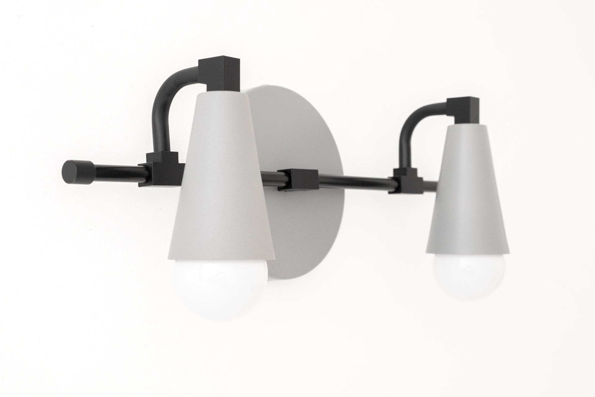 Black metal vanity light with two white cone-shaped shades and exposed bulbs. - VANITY LIGHT MODEL NO. 1229