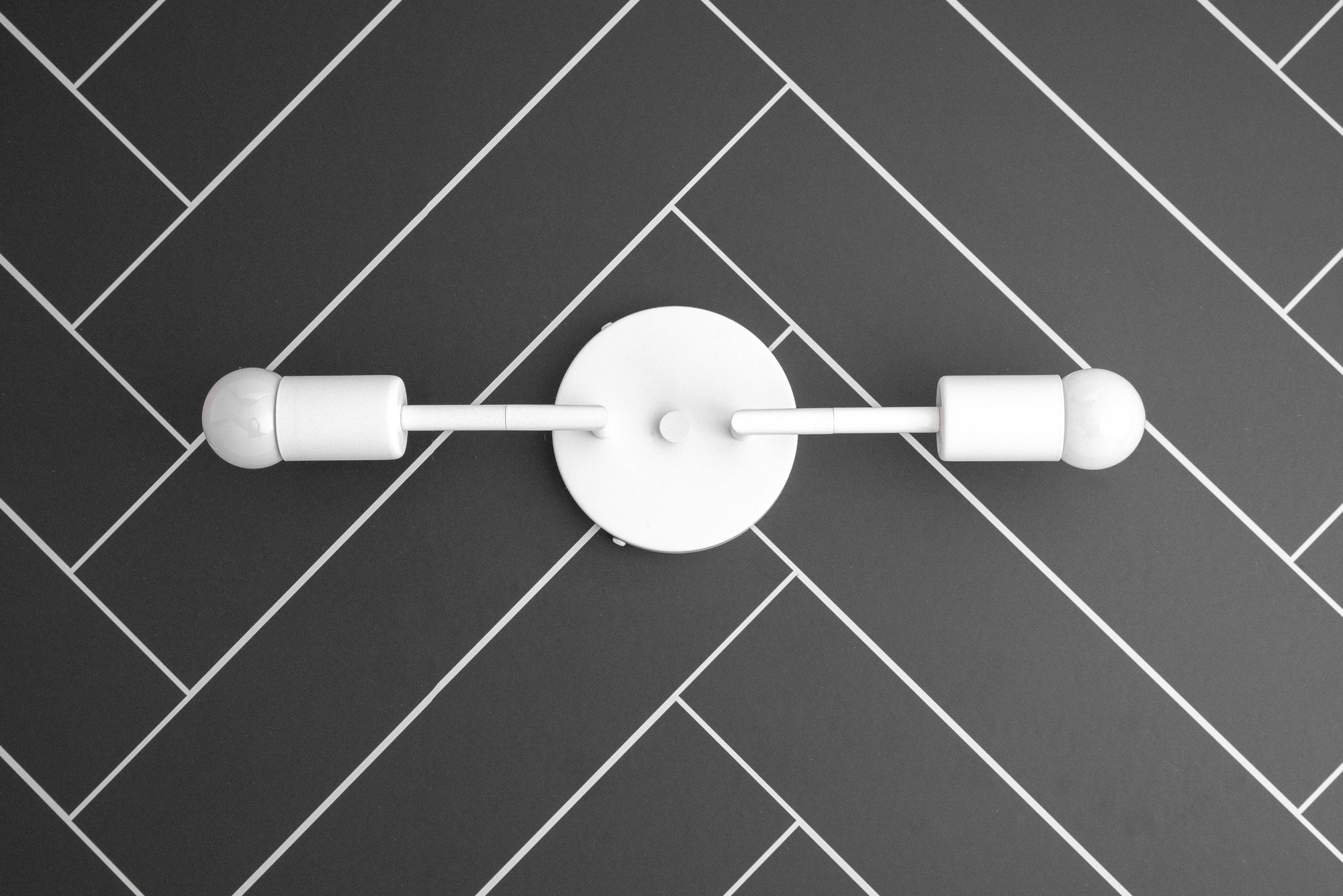 White mid-century modern two-bulb vanity light with round wall mount on black herringbone tile wall. - VANITY LIGHT MODEL NO. 1938