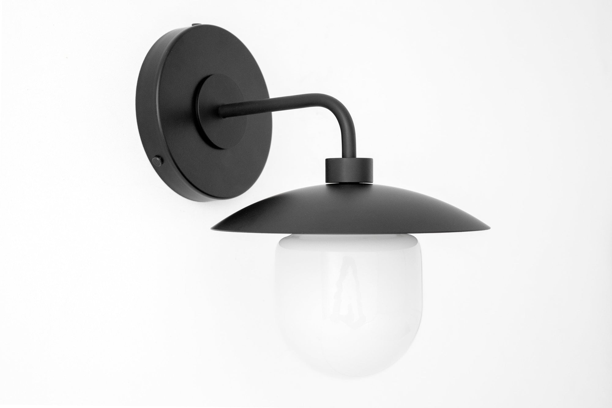 Black metal wall sconce with curved arm and matte black dome shade over frosted white glass globe. - SCONCE MODEL NO. 7039