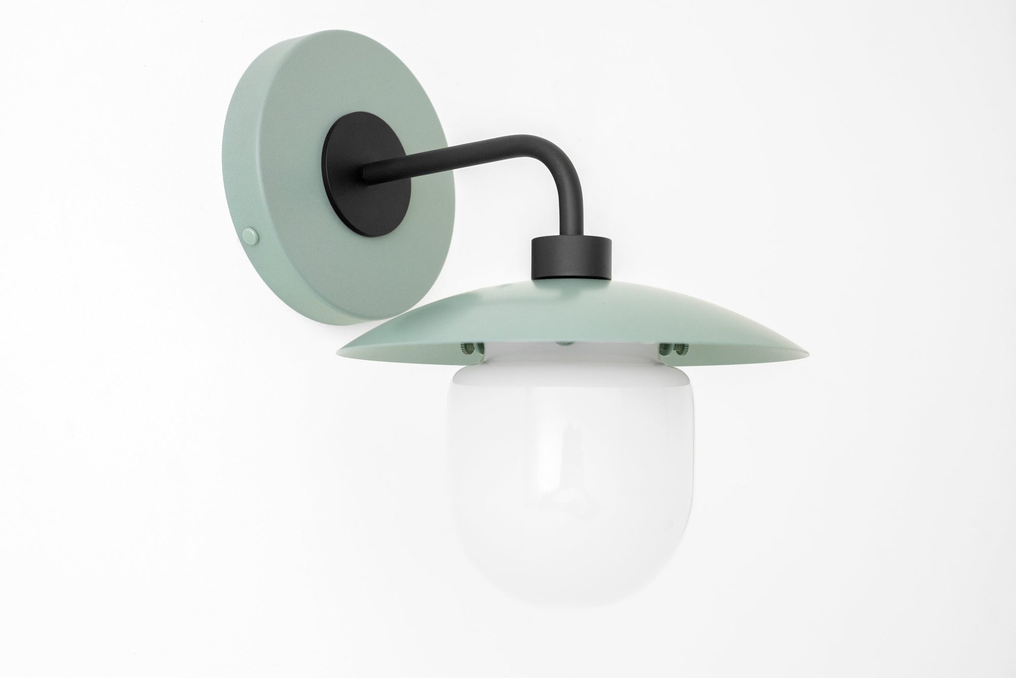 Black metal arm wall sconce with matte green round backplate and flat green shade, white globe diffuser. - SCONCE MODEL NO. 7039