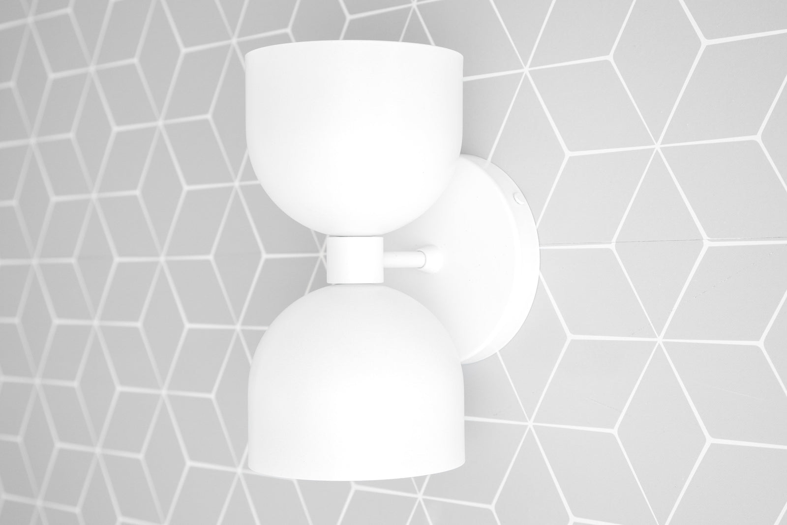 White mid-century modern up/down wall sconce with smooth rounded shades on a circular base against a geometric gray tile wall. - SCONCE MODEL NO. 5641